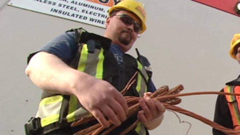 A man in a hard hat holds several spools of copper wire.