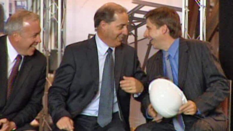 Three men, one holding a hard hat, laugh together on a platform.