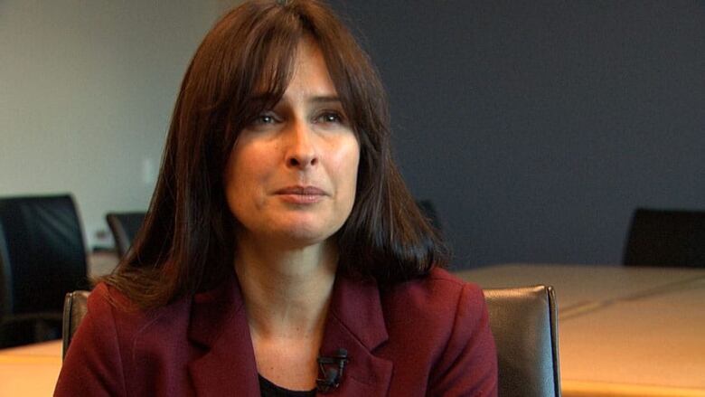 A woman with long brown hair, wearing a burgundy blazer, sits at a table.