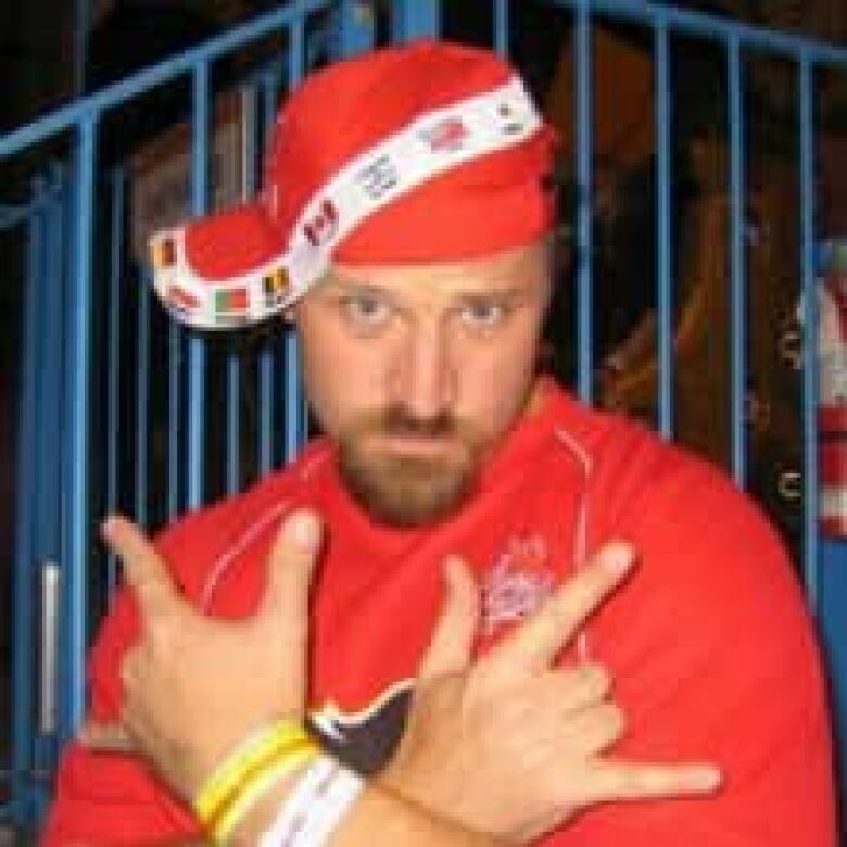 A man wearing a read jersey and cap flashes some hand signs.