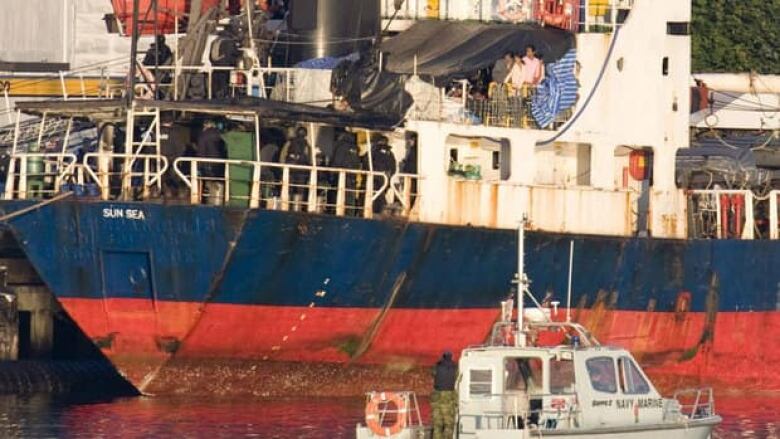 People on a ship watch as uniformed officers come on board.