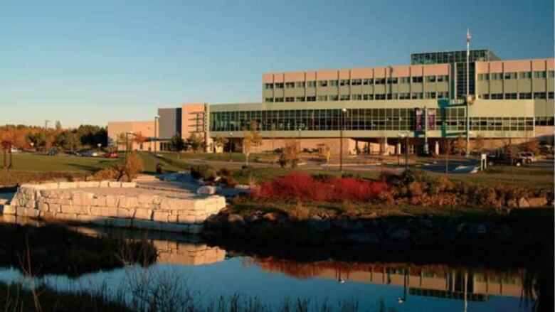 A campus building stands with green grass and a small pond in front of it.