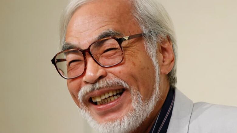 A Japanese man with glasses, laughing.