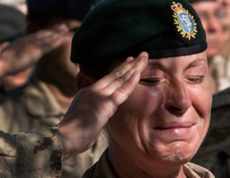 A woman in a Canadian military uniform weeps while saluting.