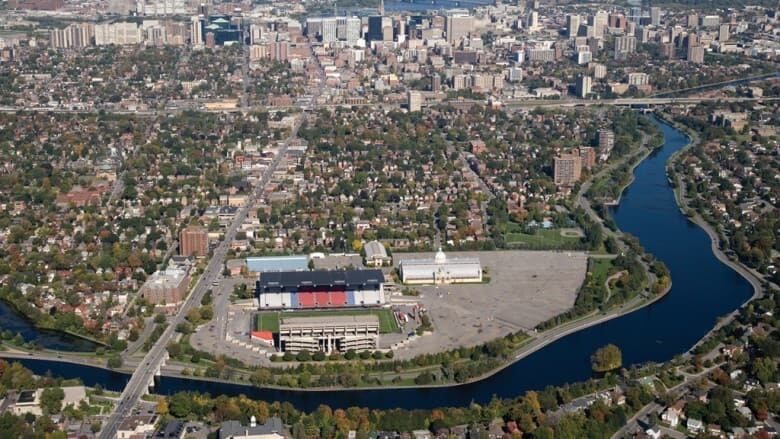 A sports stadium in a parking lot in a city, beside a canal.