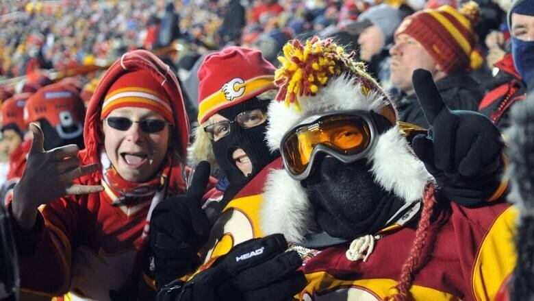 Fans dressed for winter weather with thick jackets, tuques, facemasks and goggles attend an outdoor game, sporting their team colours.