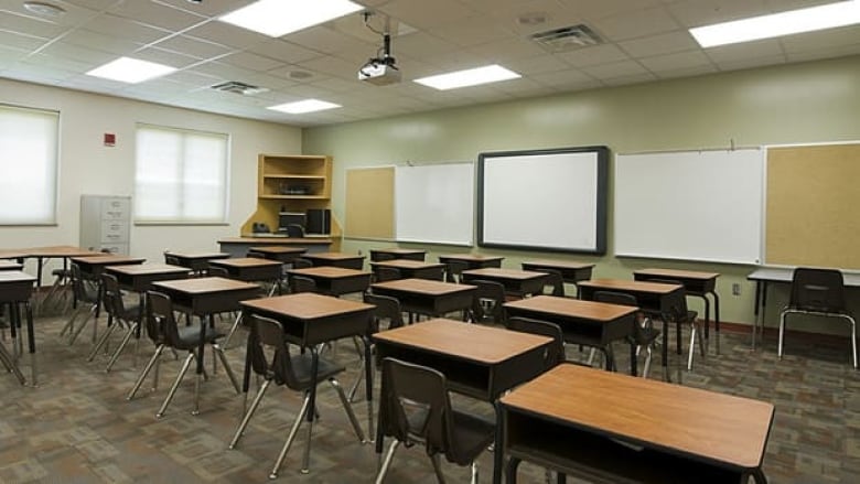 An empty classroom is seen from the back, looking toward the white board