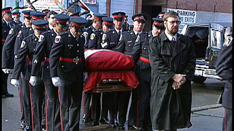 Police officers carry a casket draped in a Canadian flag.