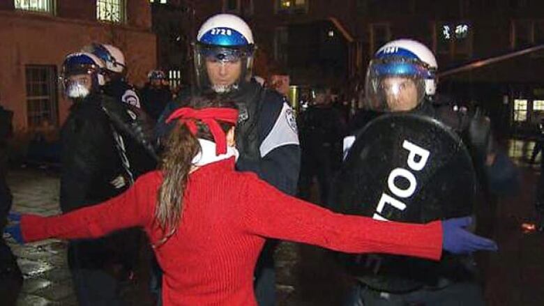 woman in red standing in front of riot police