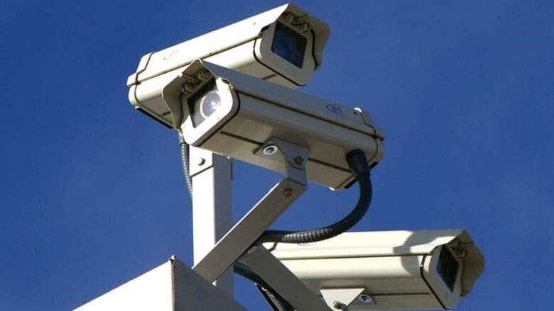 A closeup shows three surveillance cameras, pointing in different directions, mounted at the top of a post.