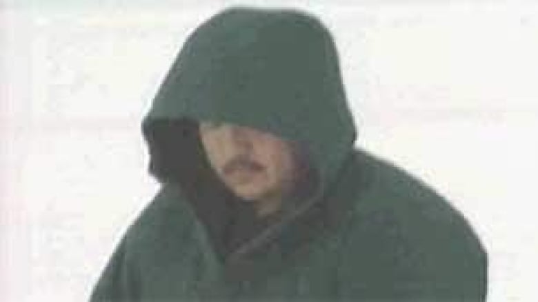 A man with a mustache wearing a hooded jacket looking down to try and hide his face