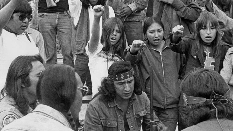 A group of people are seen holding guns and pumping their fists in the air in this black and white photo.