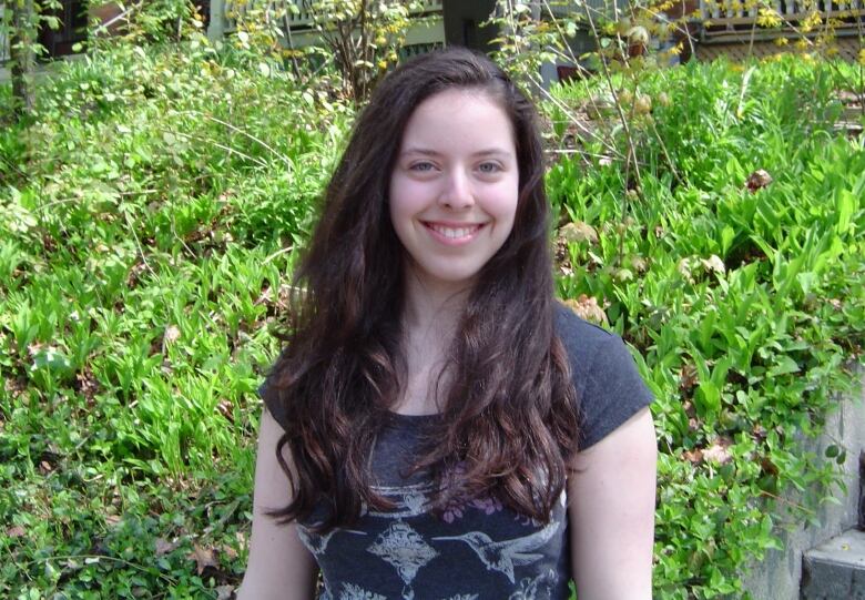 A photo of a smiling woman in front of greenery.