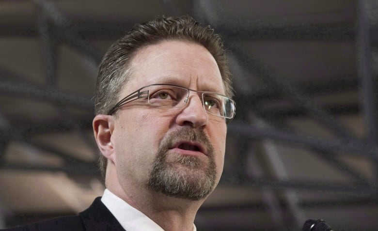 A bearded man speaks in a large auditorium.