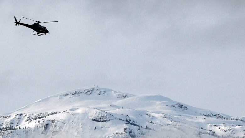 A helicopter flies upper left of the frame above a snow-covered mountaintop. 