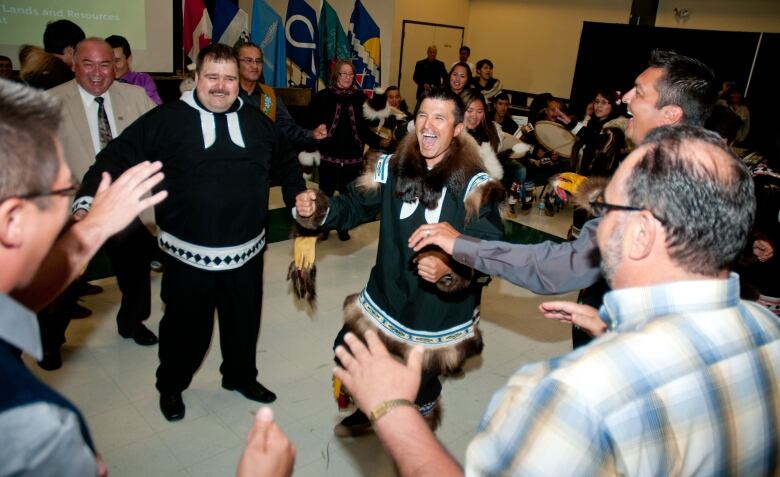 Men, some in traditional clothing, with gleeful expressions in a room. 