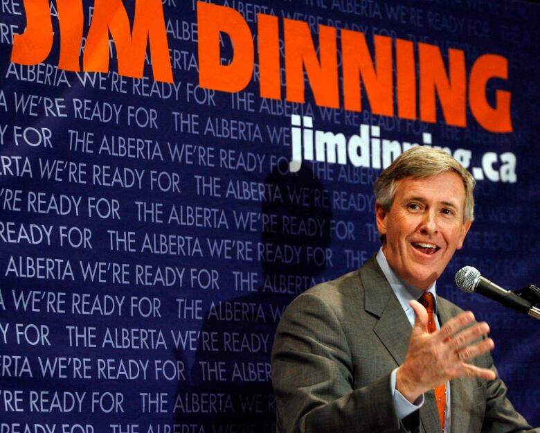 A man speaks in front of a backdrop.