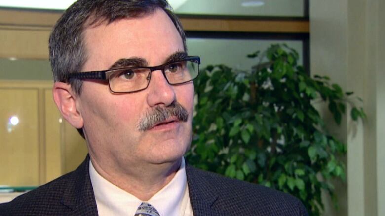 A man with a mustache wearing a suit and tie speaks to reporter.