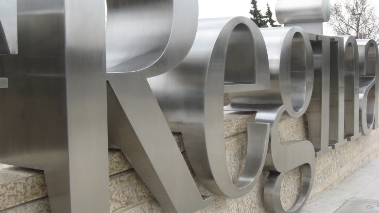 A closeup shows a sign made of large silver letters reading 