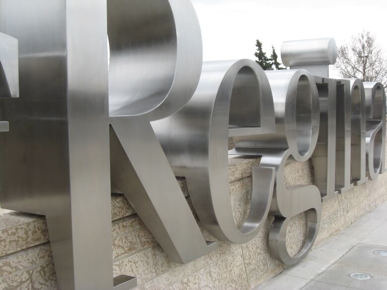 A closeup shows a sign made of large silver letters reading 