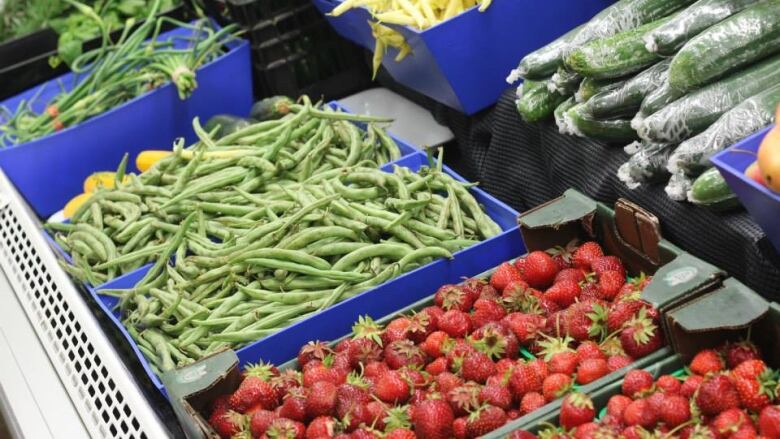 Green beans, strawberries and English cucumbers sit in blue bins in a close-up of a grocery produce display