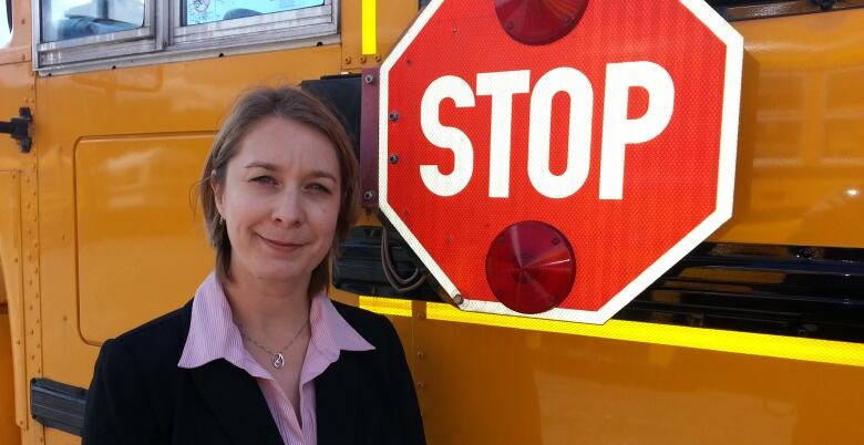 A woman posing in front of a school bus.