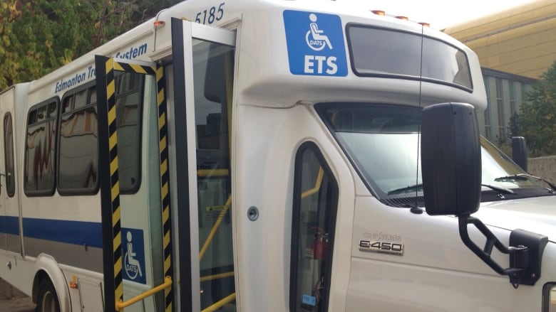 A white and blue bus is parked on a street with door open. 