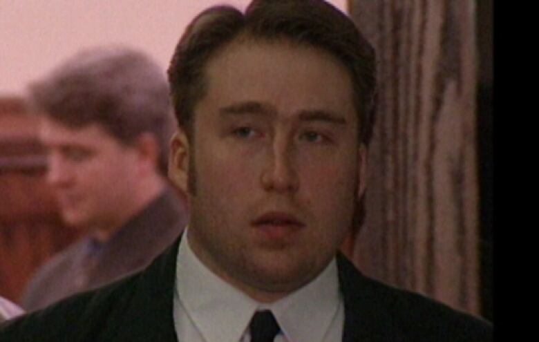 A man with long sideburns who is wearing a suit and tie walks through a courthouse.