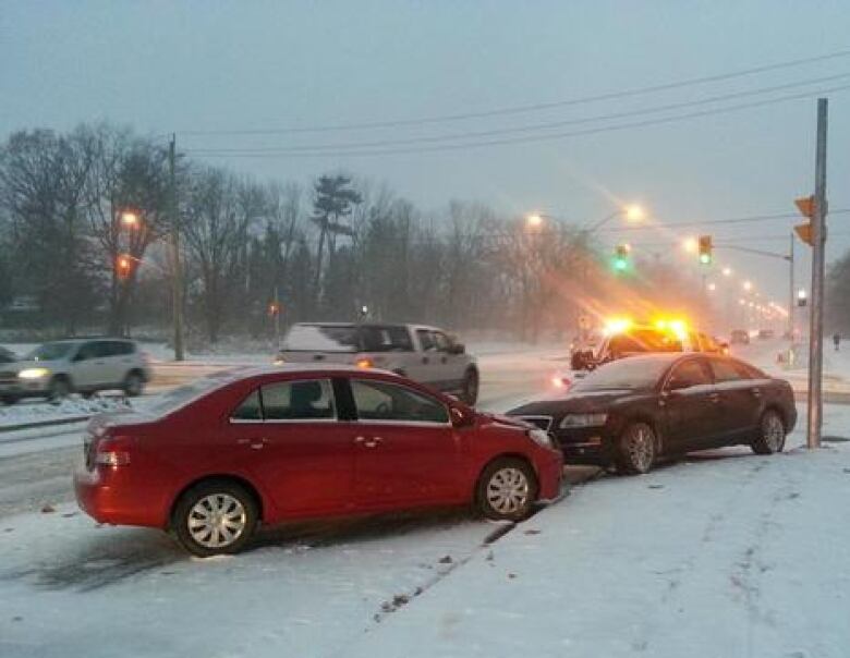 Two cars are facing each other on the side of a road after colliding during a snowstorm.