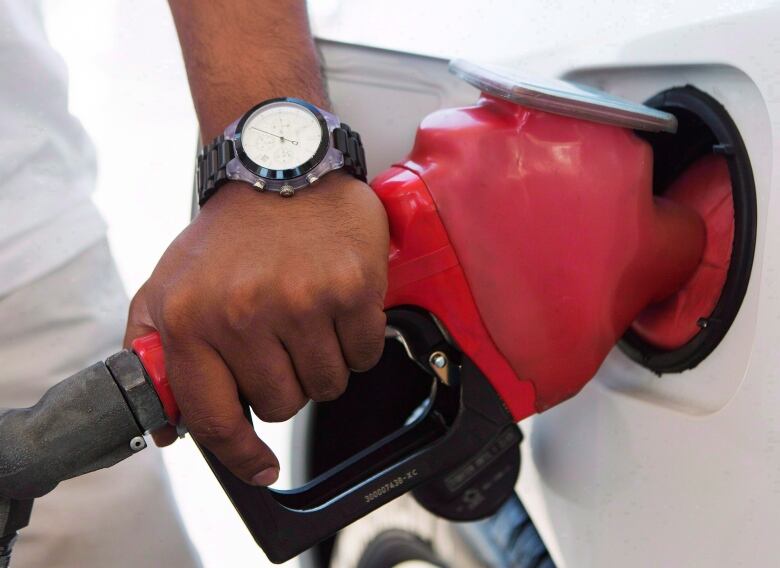 A hand rests on a gas pump while it fills a car with gasoline.