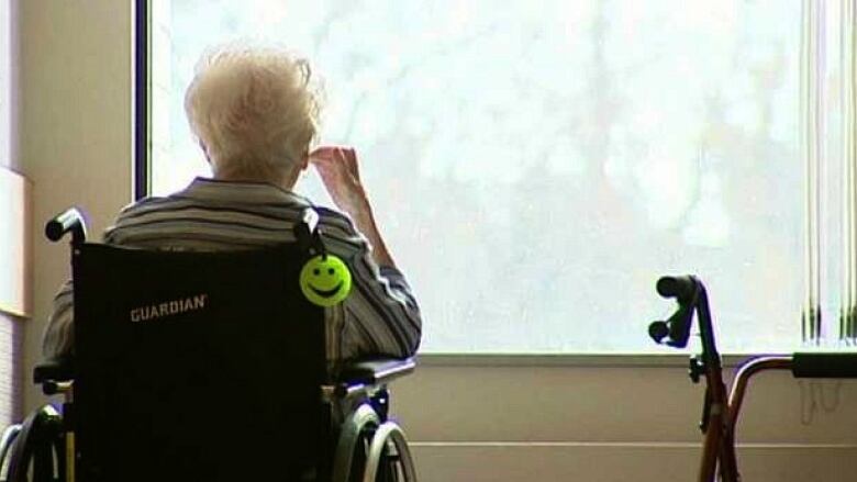 The back of an elderly woman sitting in a wheelchair, looking out a window.