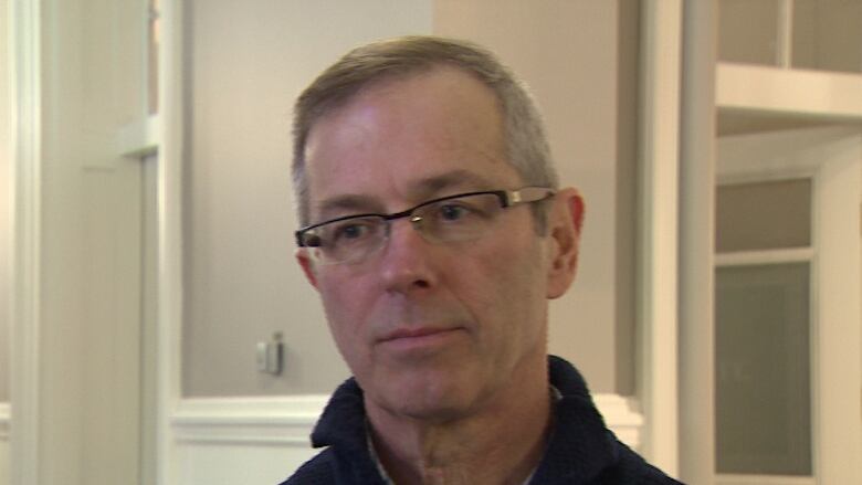 A white man with glasses stands in a hallway