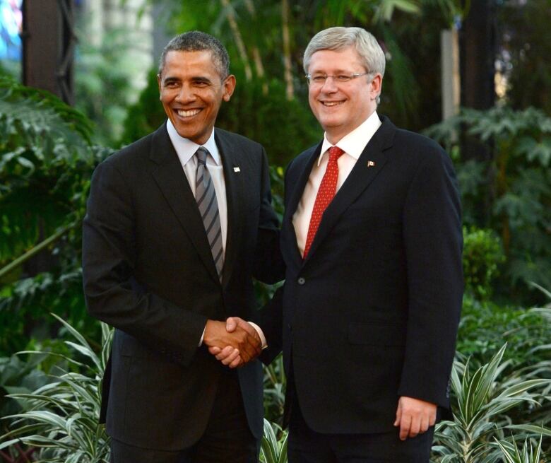 Two men wearing suits smile and shake hands