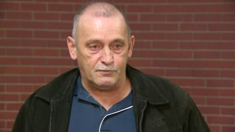 a man stands in front of a brick wall speaking to reporters 