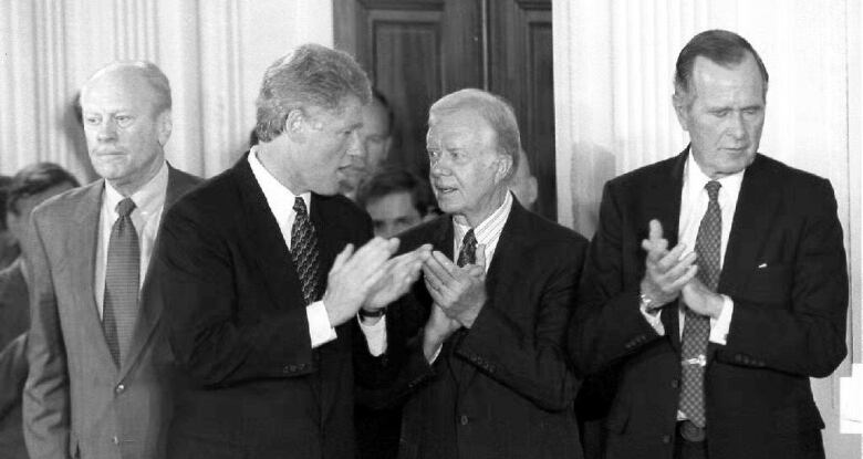 Four ex-U.S. presidents standing together and clapping.