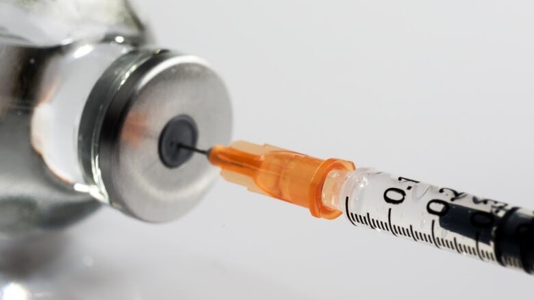 A needle dipped into a bottle of medicine against a white backdrop.