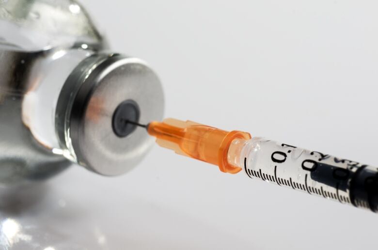 A needle dipped into a bottle of medicine against a white backdrop.