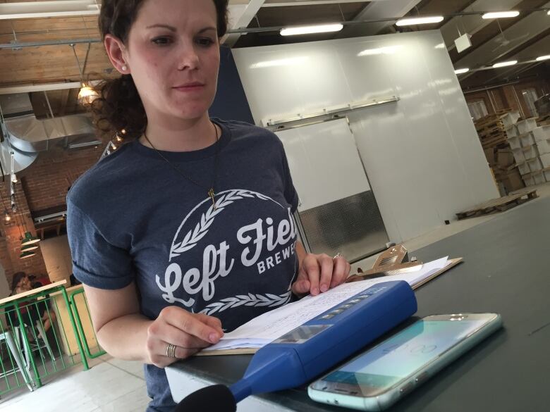 Murphy is shown wearing a Left Field Brewery t-shirt, with a clip board and phone in front of her on a table.