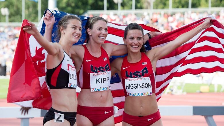 Three women posing together with a Canadian and U.S.A. flag held up behind them.