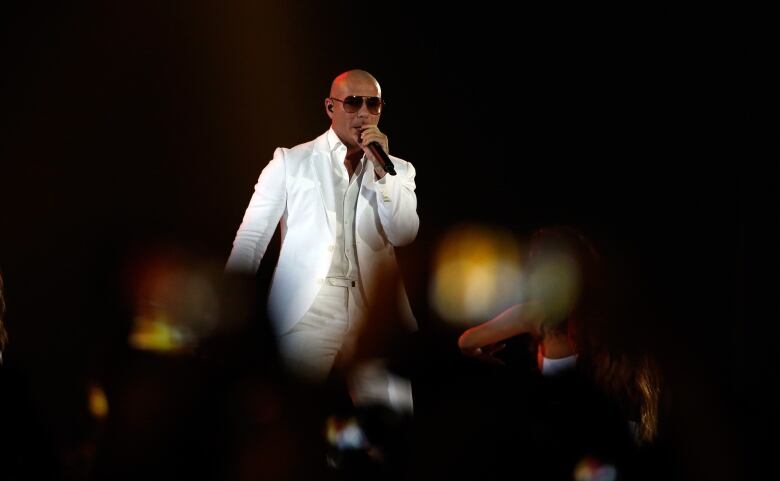 Man in white suit and sunglasses performs on stage for a crowd.