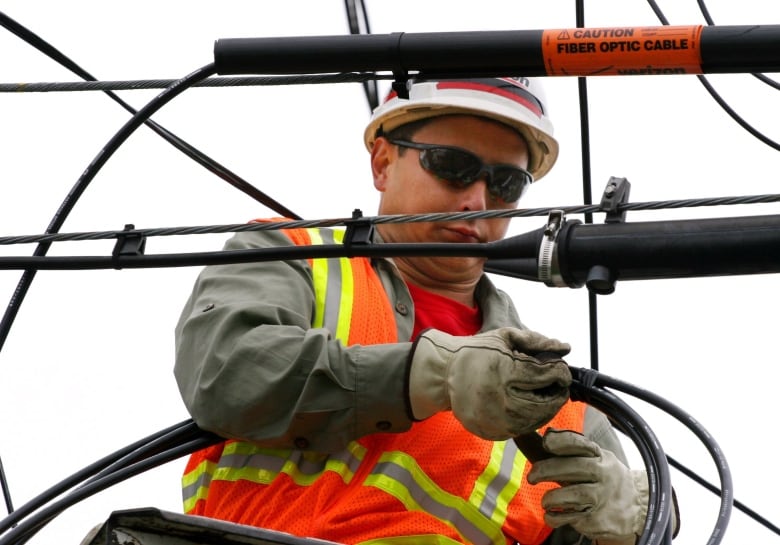 A lineman installs fiber optic cable on a telephone pole