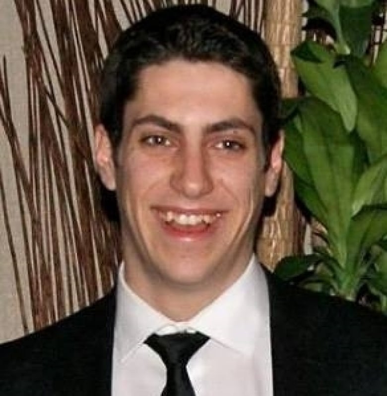 A young man with short brown hair wears a suit and tie.