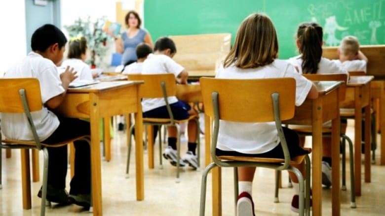 Children sit in a classroom looking at a green board. 