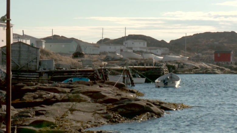 Boats are shown in the water near rocks with houses in the background. 