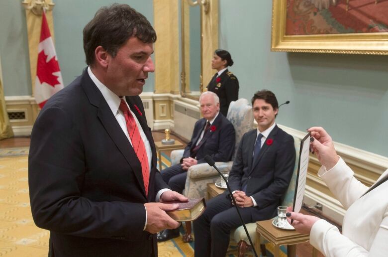 Person in a suit and a red tie reading a paper.