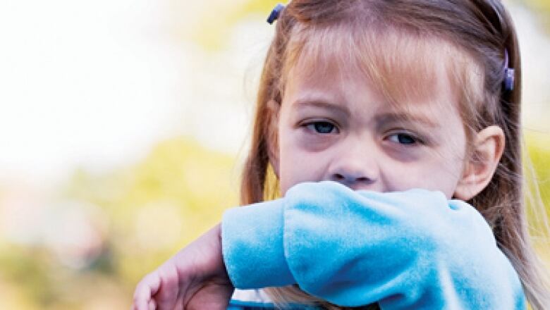 A young girl covers her mouth with her arm as she coughs.