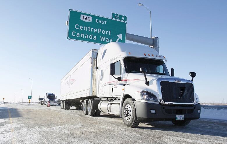 A semi-truck is driving under a sign that reads 