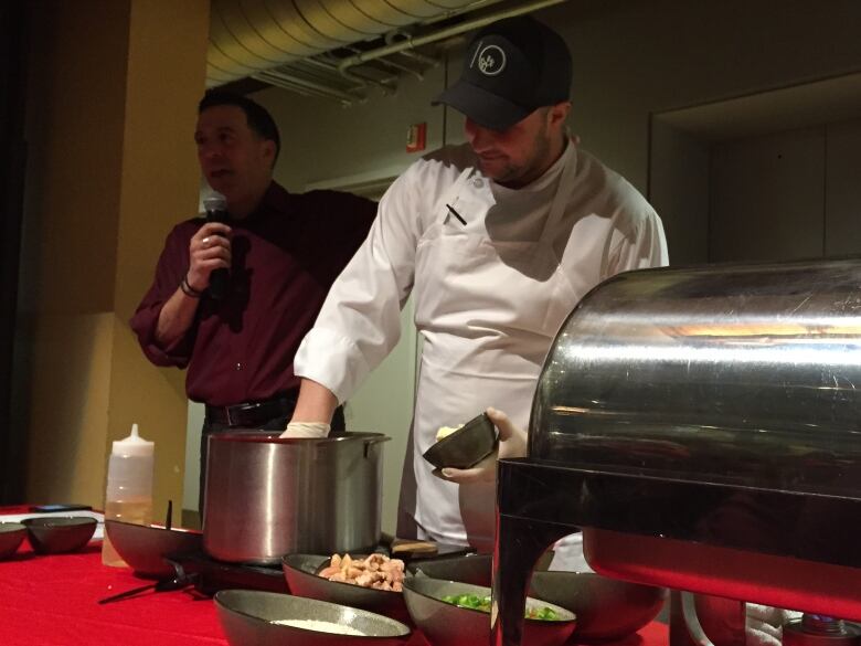 Man in chef's coat makes a dish while being interviewed during a live show