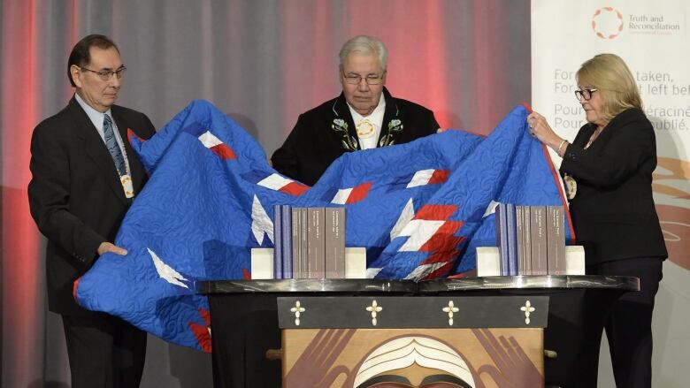 Three people remove a blanket to unveil a series of reports 