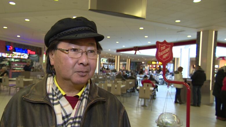 a man in a dark jacket and hat stands in a food court